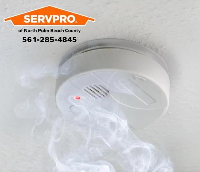 White smoke alarm with smoke on a white ceiling.